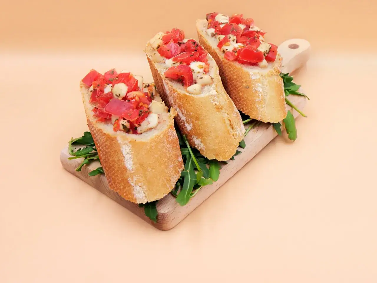 Trzy chrupiące kromki bagietki z pomidorami i mozzarellą, ułożone na desce z rukolą. Idealna bruschetta na letni wieczór.