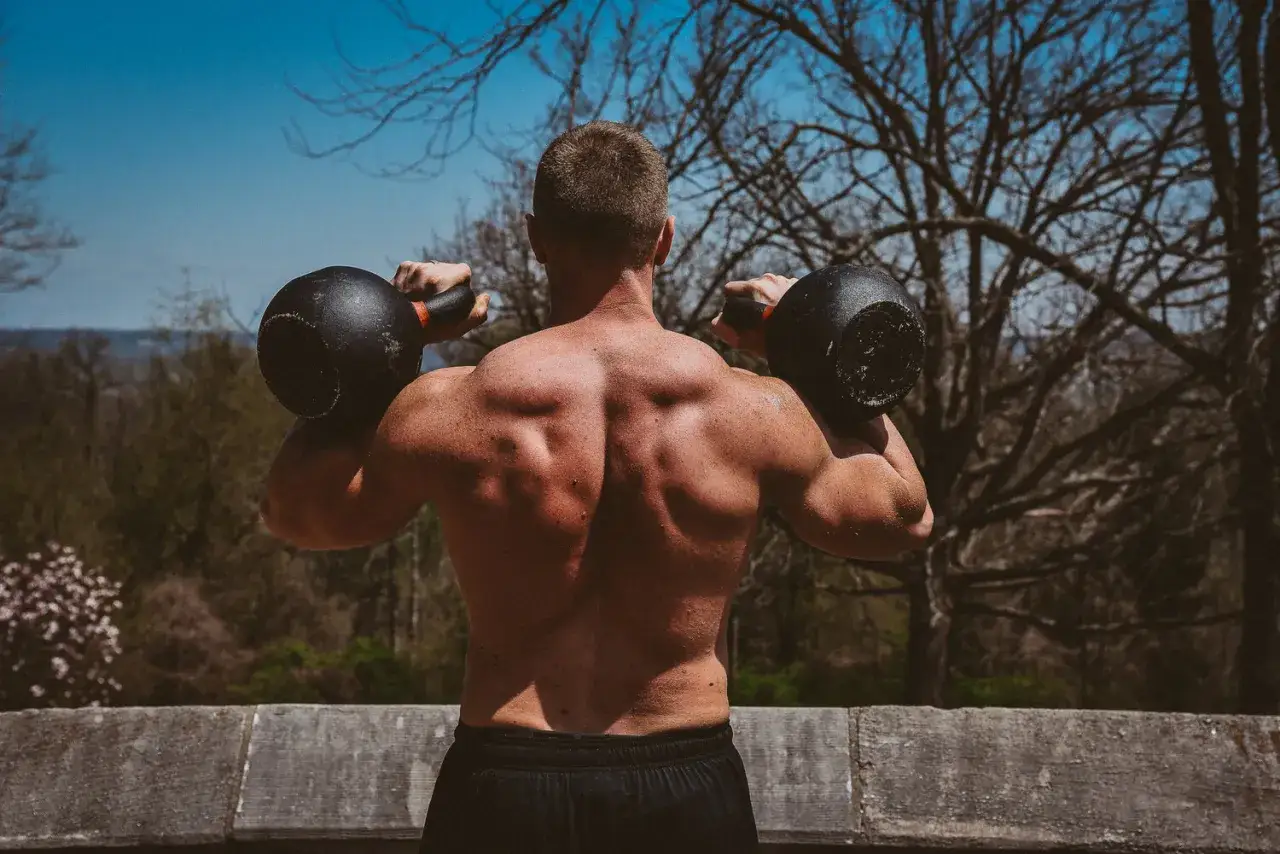 Muskul&ouml;s man utf&ouml;r kettlebell press utomhus. Tr&auml;nar axlar och rygg med tv&aring; tunga vikter.