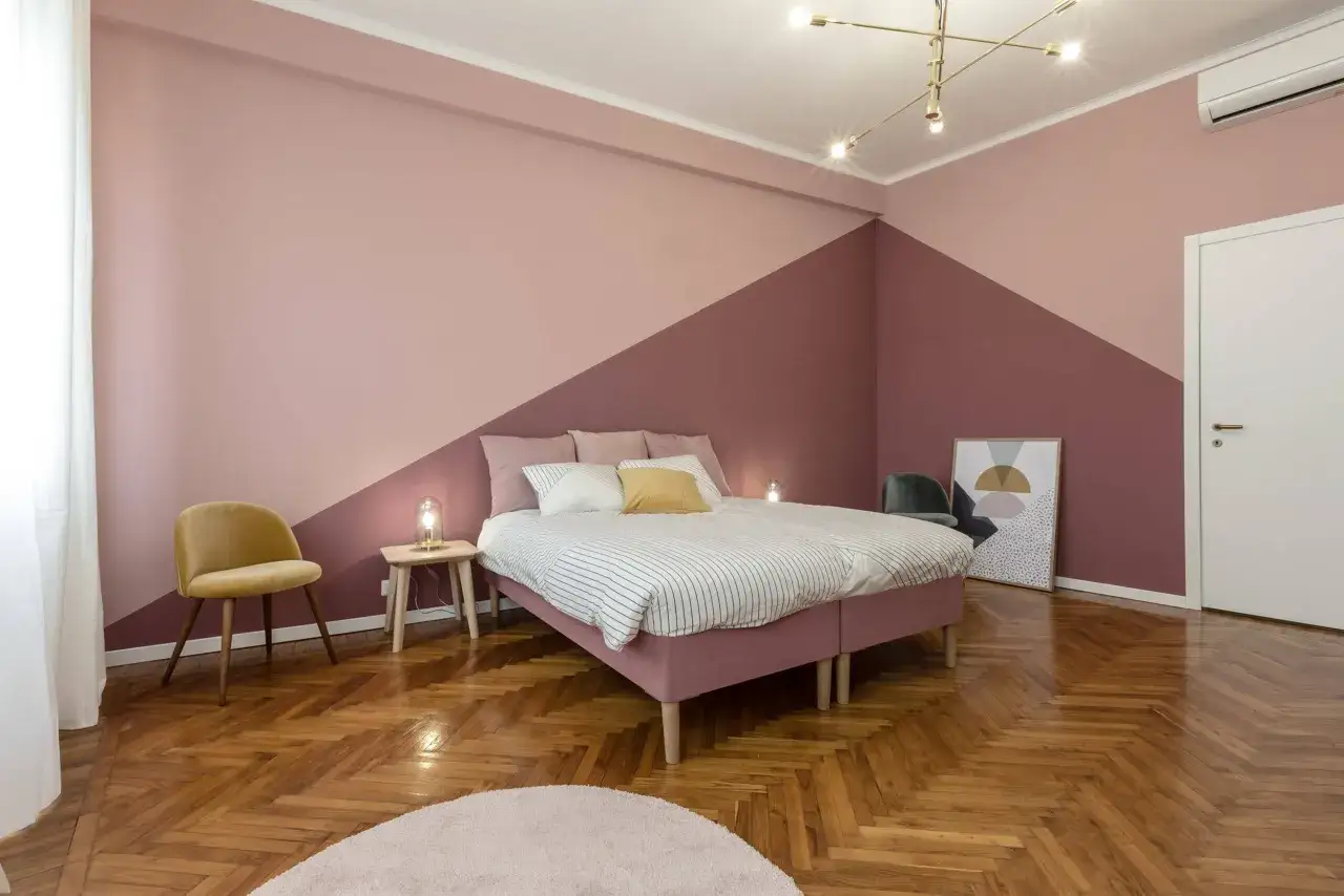 Camera da letto con pareti dipinte in due tonalità di rosa, con un motivo geometrico che divide le due sfumature.