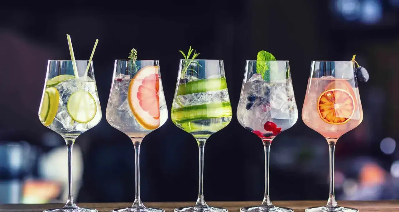 Pięć orzeźwiających drinków z ginem, udekorowanych owocami i ziołami, czeka na spróbowanie.