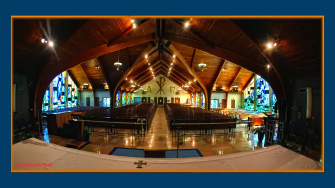 Interior of St. Benedict the Abbot Church, featuring rows of wooden pews, stained glass windows, and a vaulted wooden ceiling.