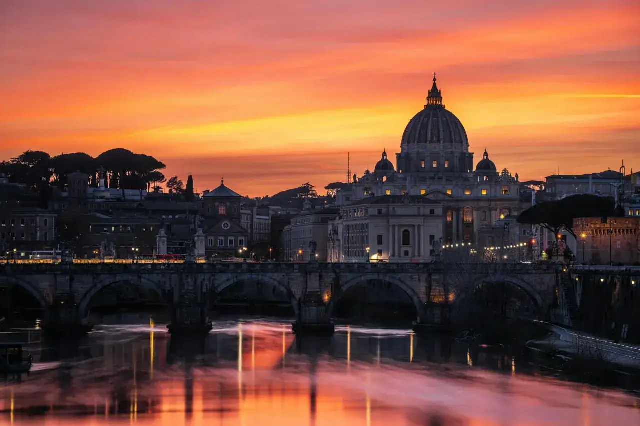 Tramonto infuocato su Roma, con San Pietro e Ponte Sant'Angelo riflessi sul Tevere. Il clima è magico.