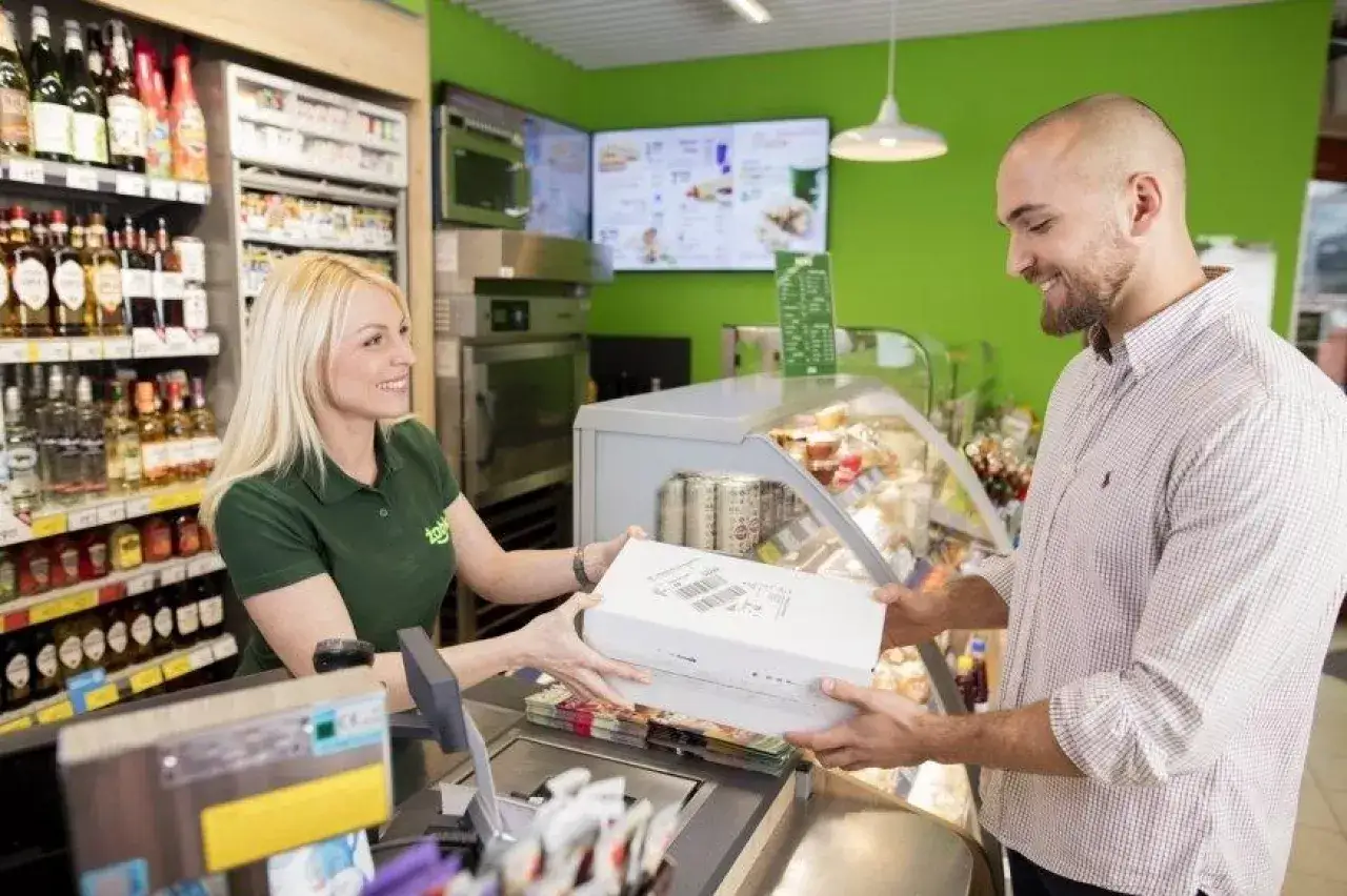 Uśmiechnięta sprzedawczyni przekazuje klientowi paczkę w ramach usługi click and collect.