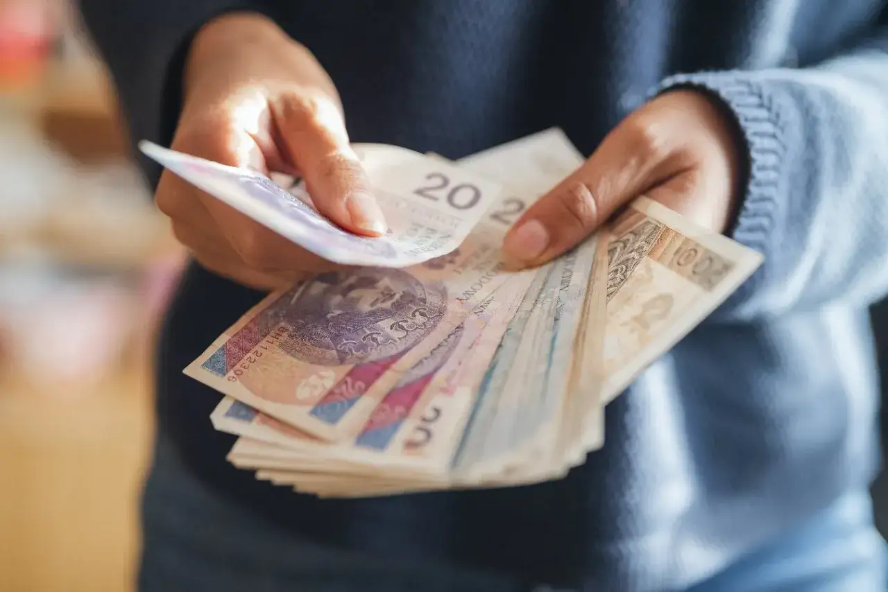 Dłonie liczą banknoty złotowe, zastanawiając się, ile wzrośnie emerytura z OFE po 65 roku życia.