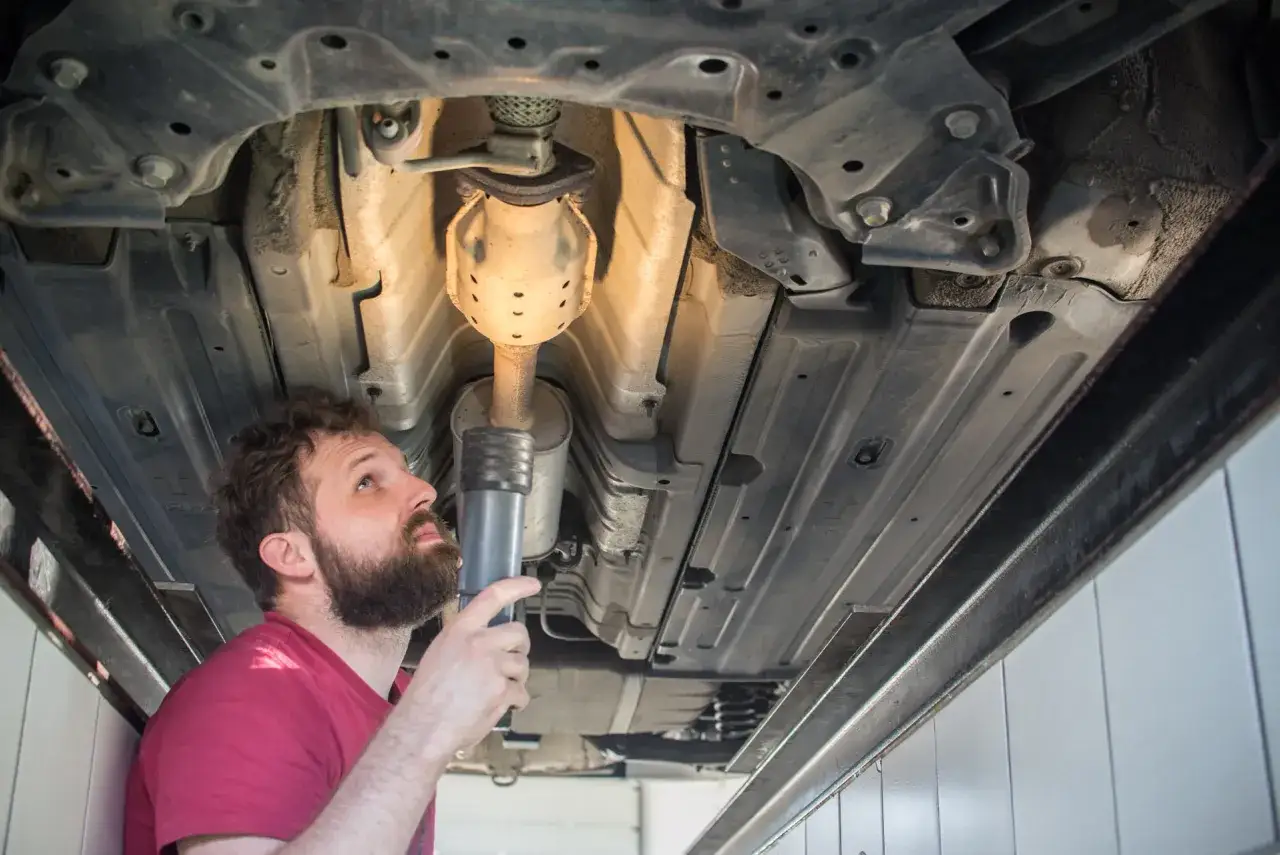 Mechanik z latarką bada podwozie auta, szukając dziury w tłumiku.