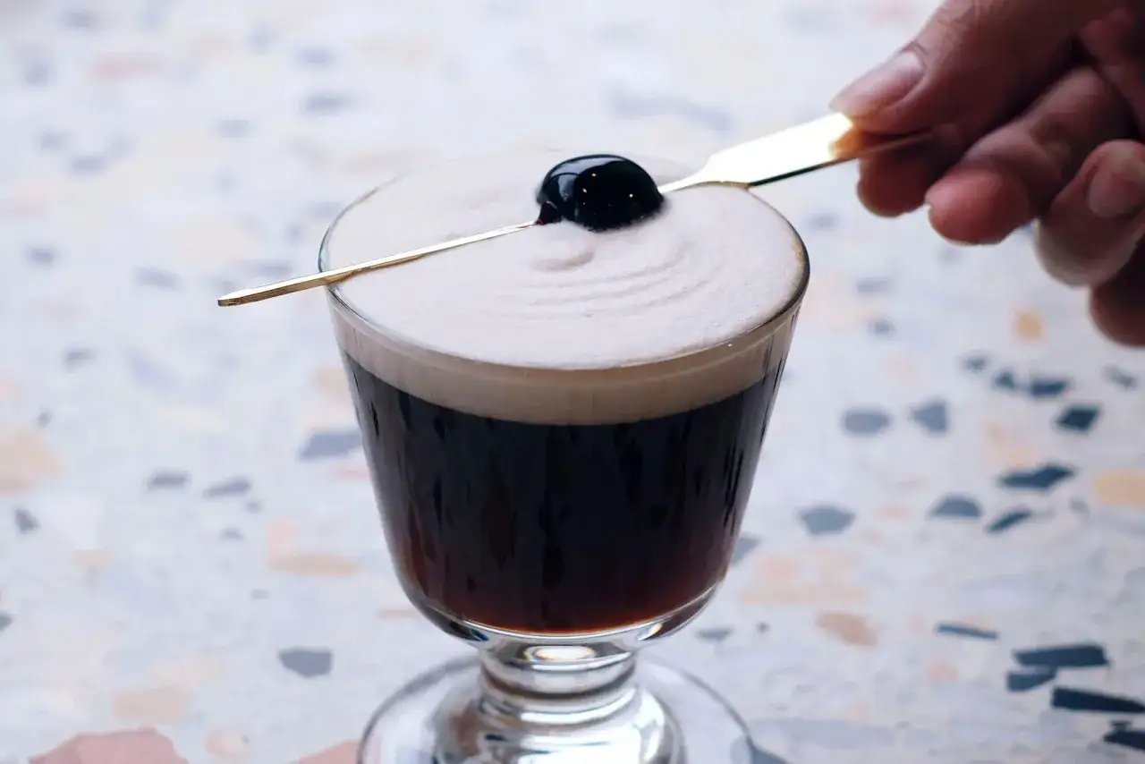 Ein k&ouml;stlicher Kaffee-Cocktail mit cremigem Schaum und einer Kirsche, garniert mit einem goldenen Spie&szlig;.