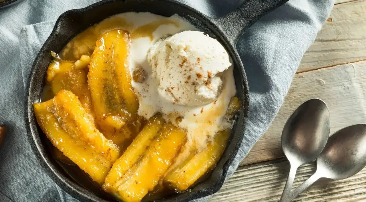 Délicieuse banane flambée servie dans une poêle en fonte avec une boule de glace à la vanille saupoudrée de cannelle.