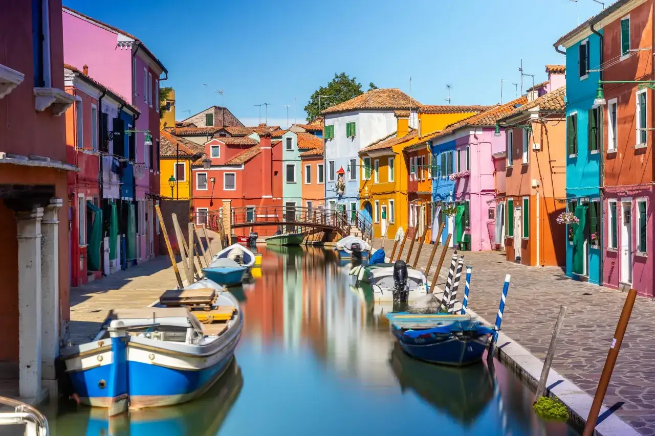 Canal de Venise bord&eacute; de maisons color&eacute;es, reflets vibrants dans l'eau, bateaux amarr&eacute;s.