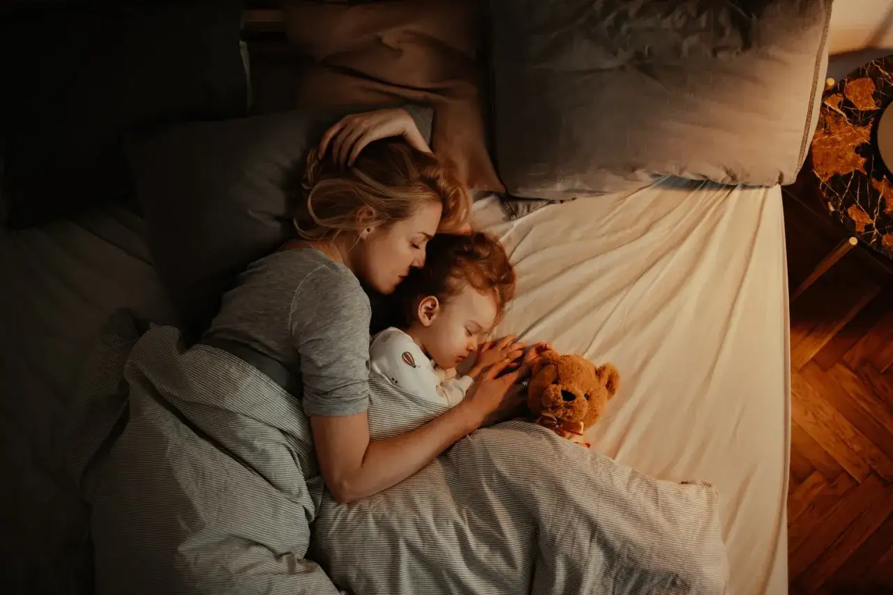 Mutter und Kind schlafen eng umschlungen. Ab wann Babys bewusst kuscheln, zeigt diese Szene der Geborgenheit.