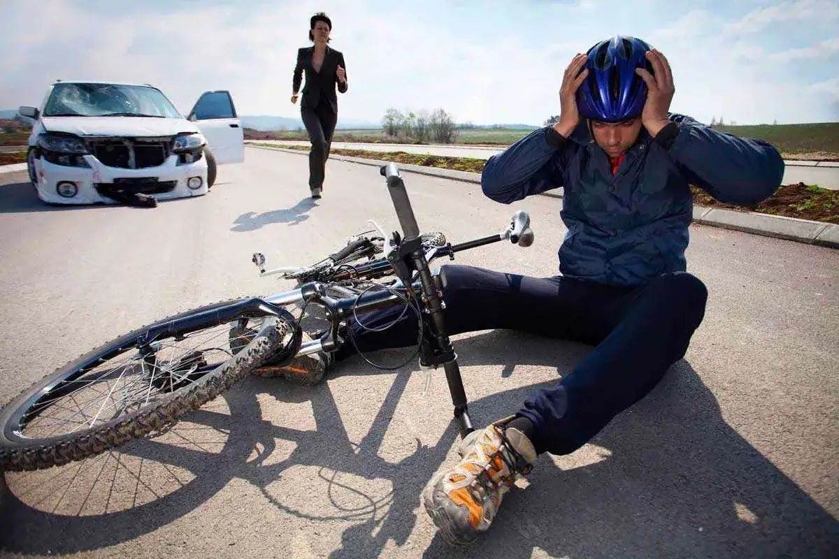 Ciclista a terra con bici rovesciata dopo un **infortunio in itinere**. Auto danneggiata e donna in fuga.