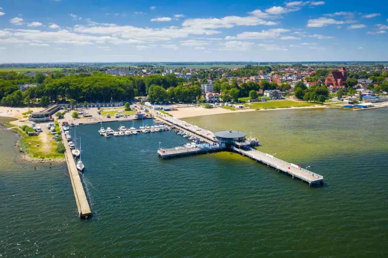 Widok na zatokę pucką z molo, mariną pełną jacht&oacute;w i nadmorskim miasteczkiem w tle.