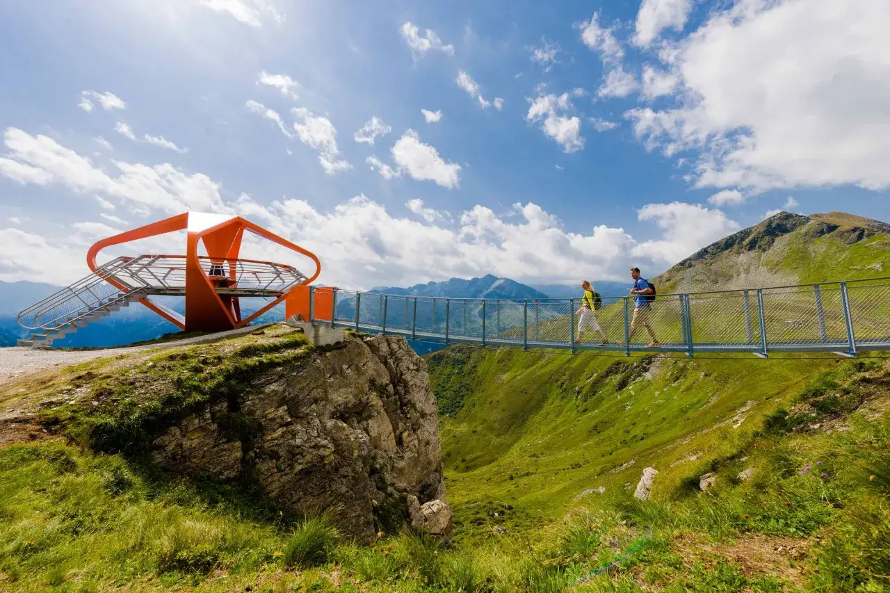 Två vandrare njuter av en fantastisk utsikt från en hängbro i Bad Gastein. En modern orange utsiktsplattform syns till vänster.