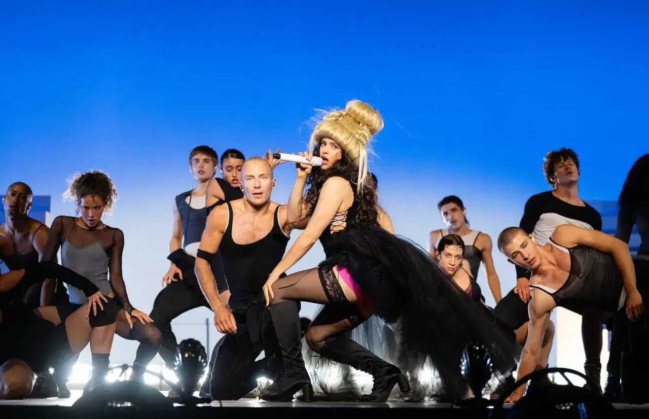 Rosalía, la cantante spagnola, domina il palco con un microfono, circondata da ballerini in un'esibizione energica.