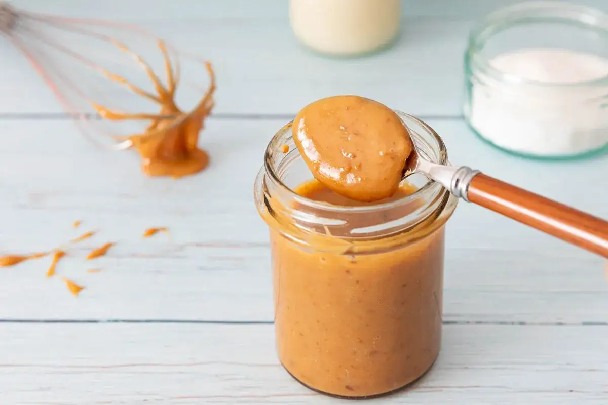 Une cuill&egrave;re de confiture de lait onctueuse est pr&eacute;lev&eacute;e d'un pot en verre. Un fouet d&eacute;gouline de cette gourmandise.