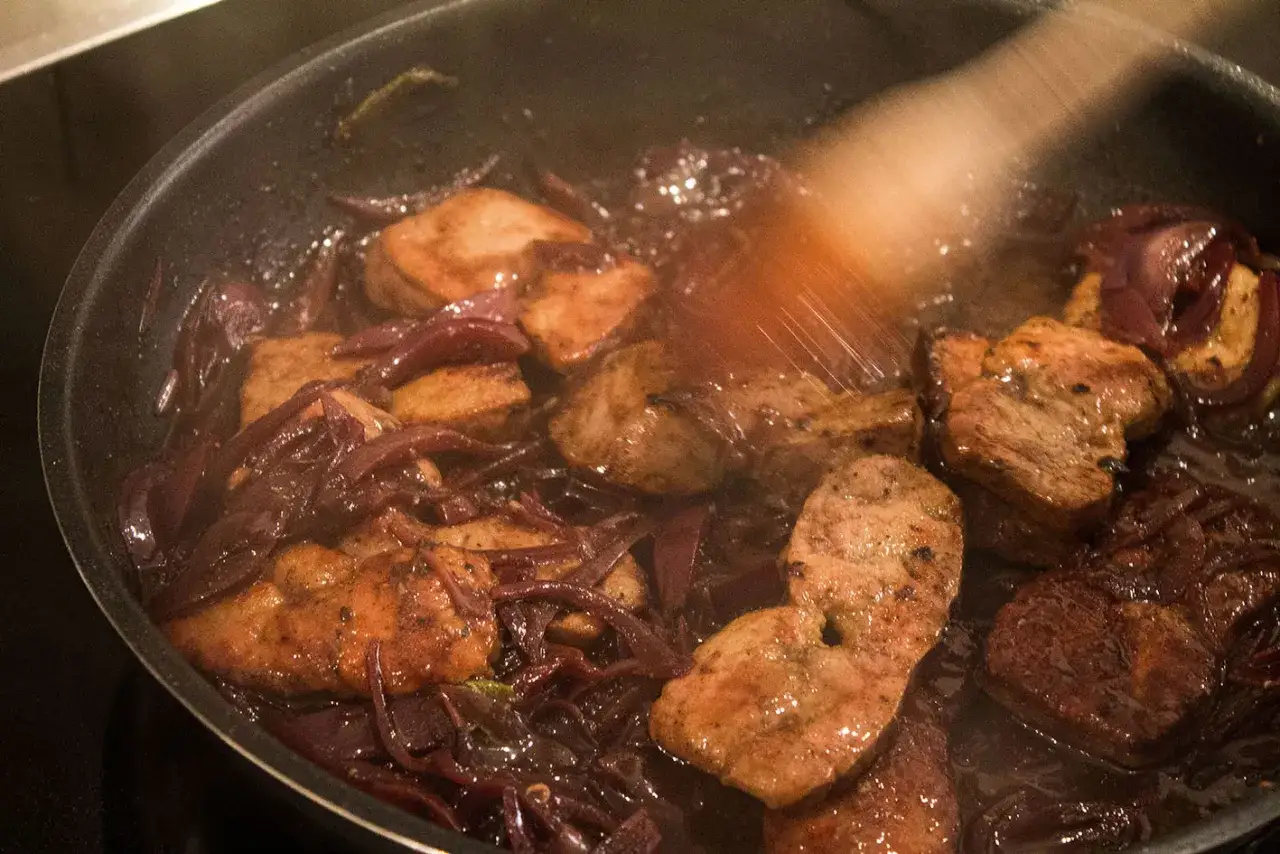 Kalbsleber rezept mit sauce: zarte Leberst&uuml;cke mit roten Zwiebeln in einer Pfanne geschmort, bereit zum Servieren.