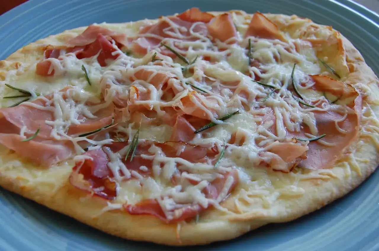 Eine köstliche Pizza Bianca mit Schinken, Käse und Rosmarin auf einem blauen Teller.
