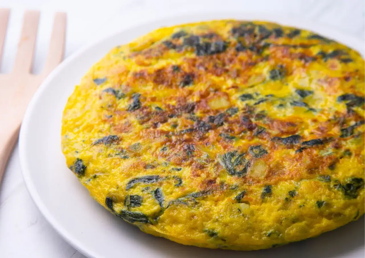 Frittata di spinaci dorata e soffice, con pezzi di spinaci ben visibili, servita su un piatto bianco.