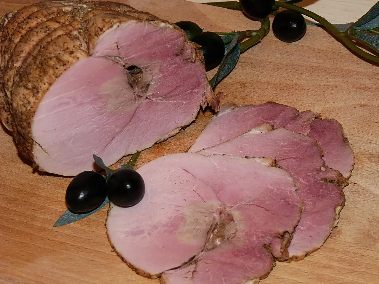 Szybkie peklowanie mięsa do pieczenia zakończone sukcesem. Soczysta szynka pokrojona w plastry, ozdobiona oliwkami.