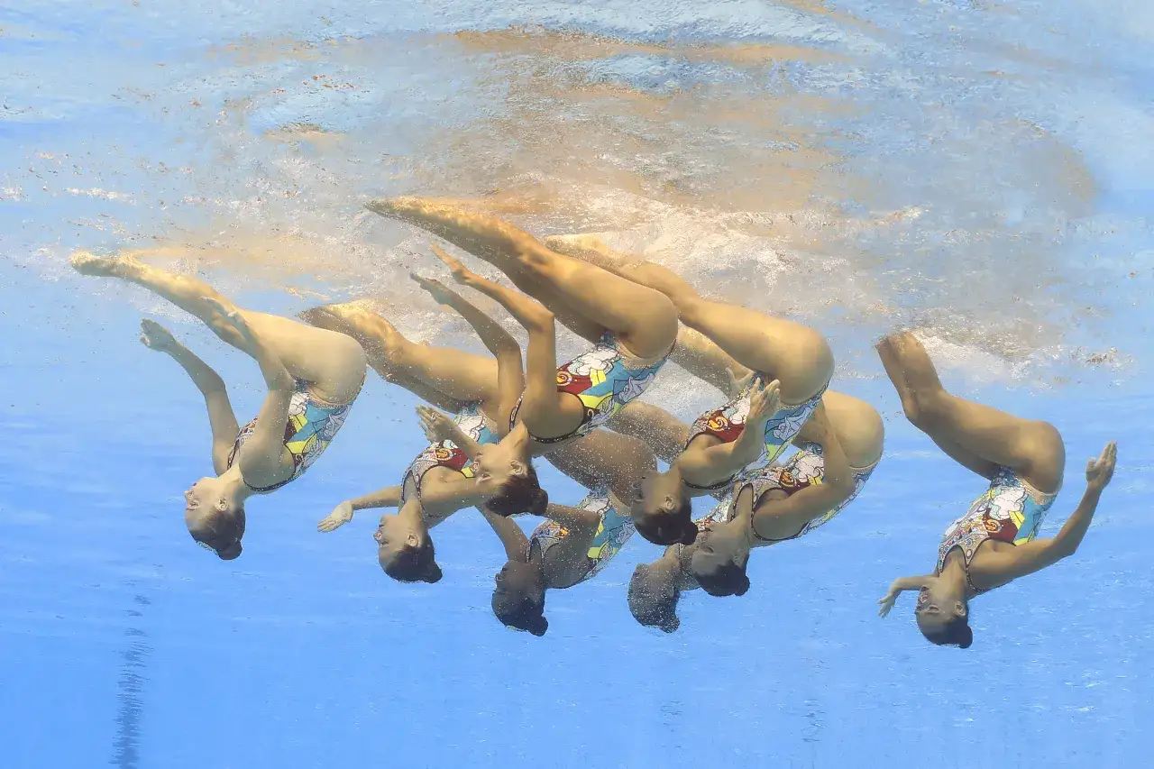 Grupa sportsmenek wykonuje skomplikowaną figurę podczas zawodów w pływaniu synchronicznym.