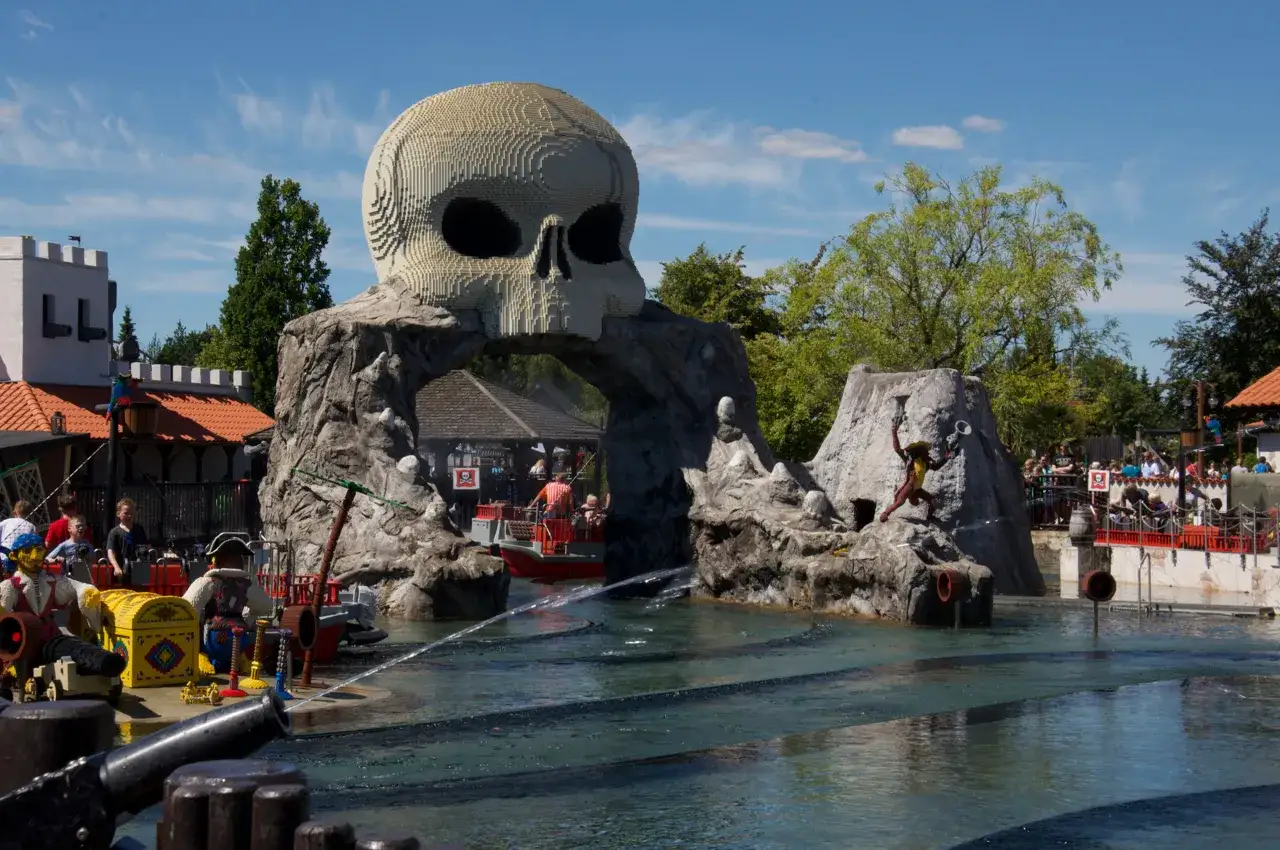 Gigantyczna czaszka z klocków LEGO w Legolandzie w Danii, nad wodną atrakcją z łodziami i piratami.