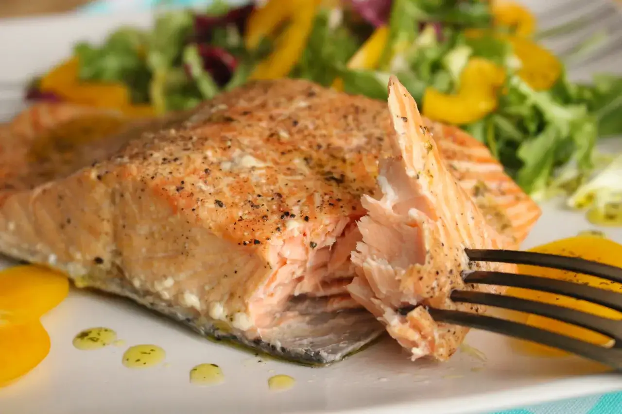 Soczysty łosoś wędzony na gorąco, lekko przyprawiony, podany z sałatką i żółtą papryką. Widok z bliska na delikatne mięso ryby.