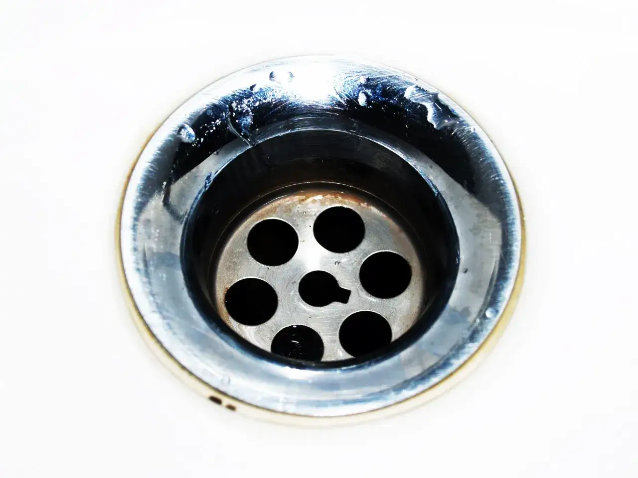 Gouttes d'eau stagnantes dans un évier bouché mais pas de bouchon visible. Le métal du siphon est sale et usé.