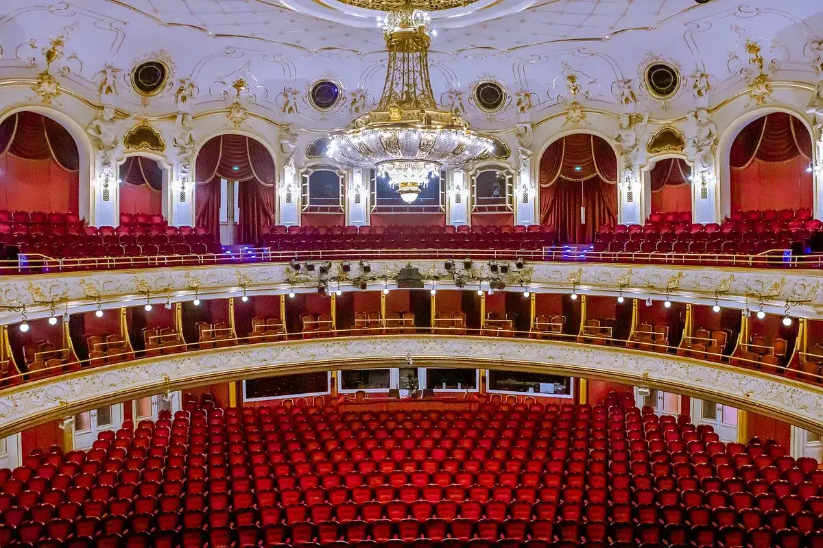 Wnętrze teatru z czerwonymi fotelami, złoceniami i kryształowym żyrandolem. Idealne miejsce na **operę i operetkę**.