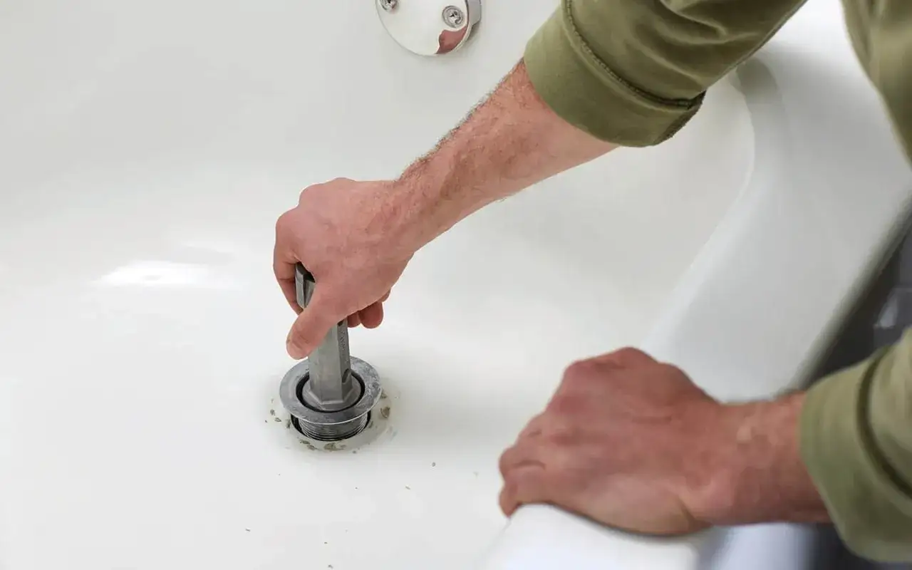 A person uses a tool to remove a bathtub drain. This shows how to remove bathtub drain for cleaning or repair.