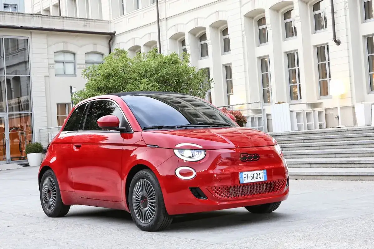 Fiat 500 rouge garée devant un bâtiment blanc. Le **pression des pneus** est parfaite pour une conduite urbaine.