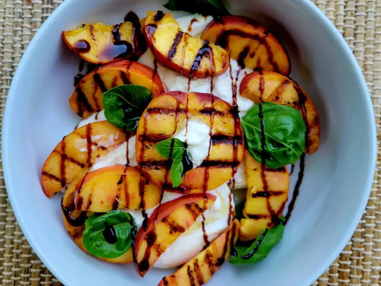 Gegrillte Pfirsichspalten auf cremigem Burrata, beträufelt mit Balsamico-Glasur und garniert mit frischem Basilikum. Ein köstlicher Pfirsich Burrata Salat.
