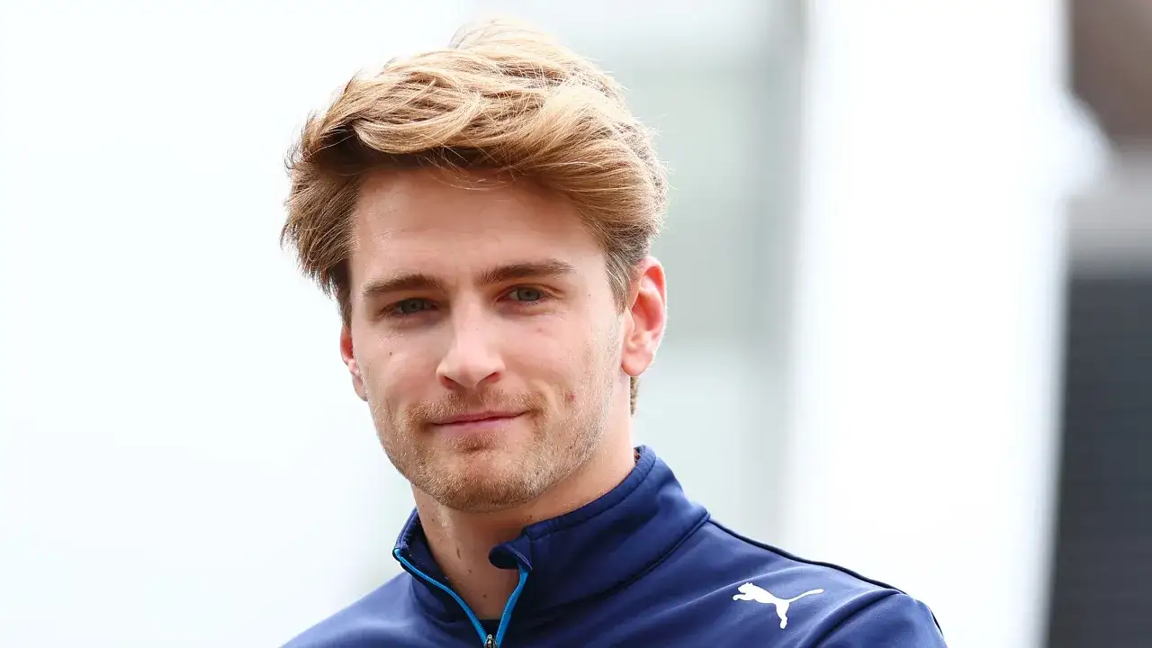 Logan Sargeant, piloto de F1, sonríe con su cabello rubio despeinado y un polo azul con el logo de Puma.
