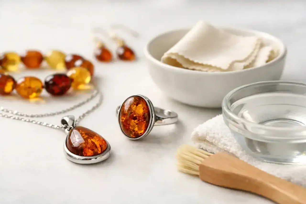 Joyas de &aacute;mbar, un anillo, collar y pulsera, junto a un cuenco con agua, un pa&ntilde;o y un cepillo, para saber como limpiar el &aacute;mbar.