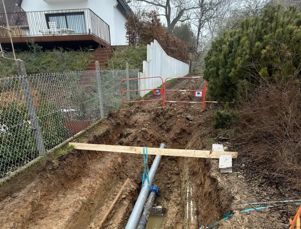 Travaux de réparation d'une fuite d'eau avant compteur. Une tranchée est creusée, révélant des tuyaux et des barrières de sécurité.
