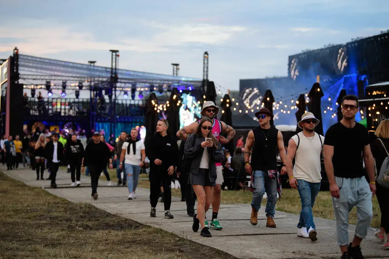 Ludzie idą na festiwal Audioriver. W tle widać scenę i światła.