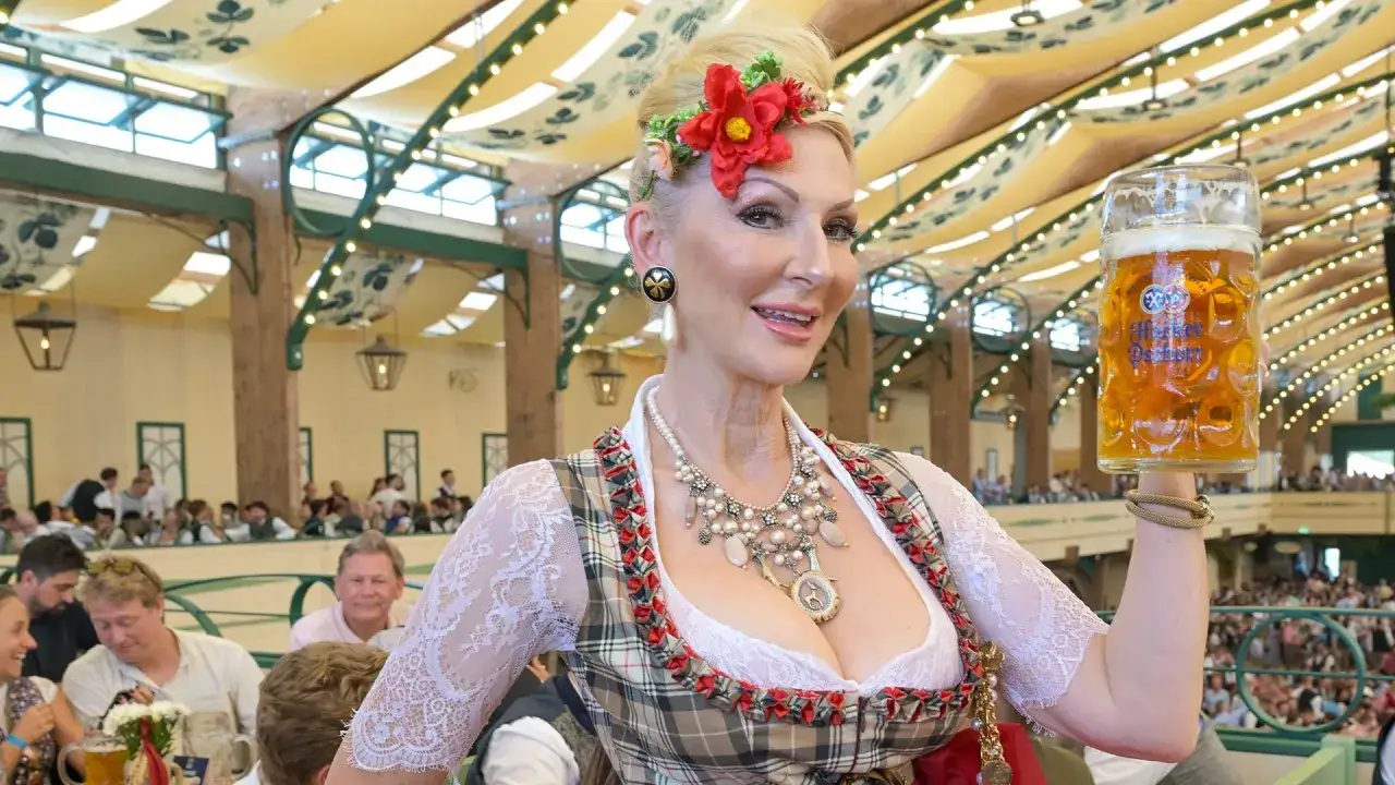 Donna in costume bavarese solleva un boccale di birra, un'immagine che evoca la storia dell'Oktoberfest.