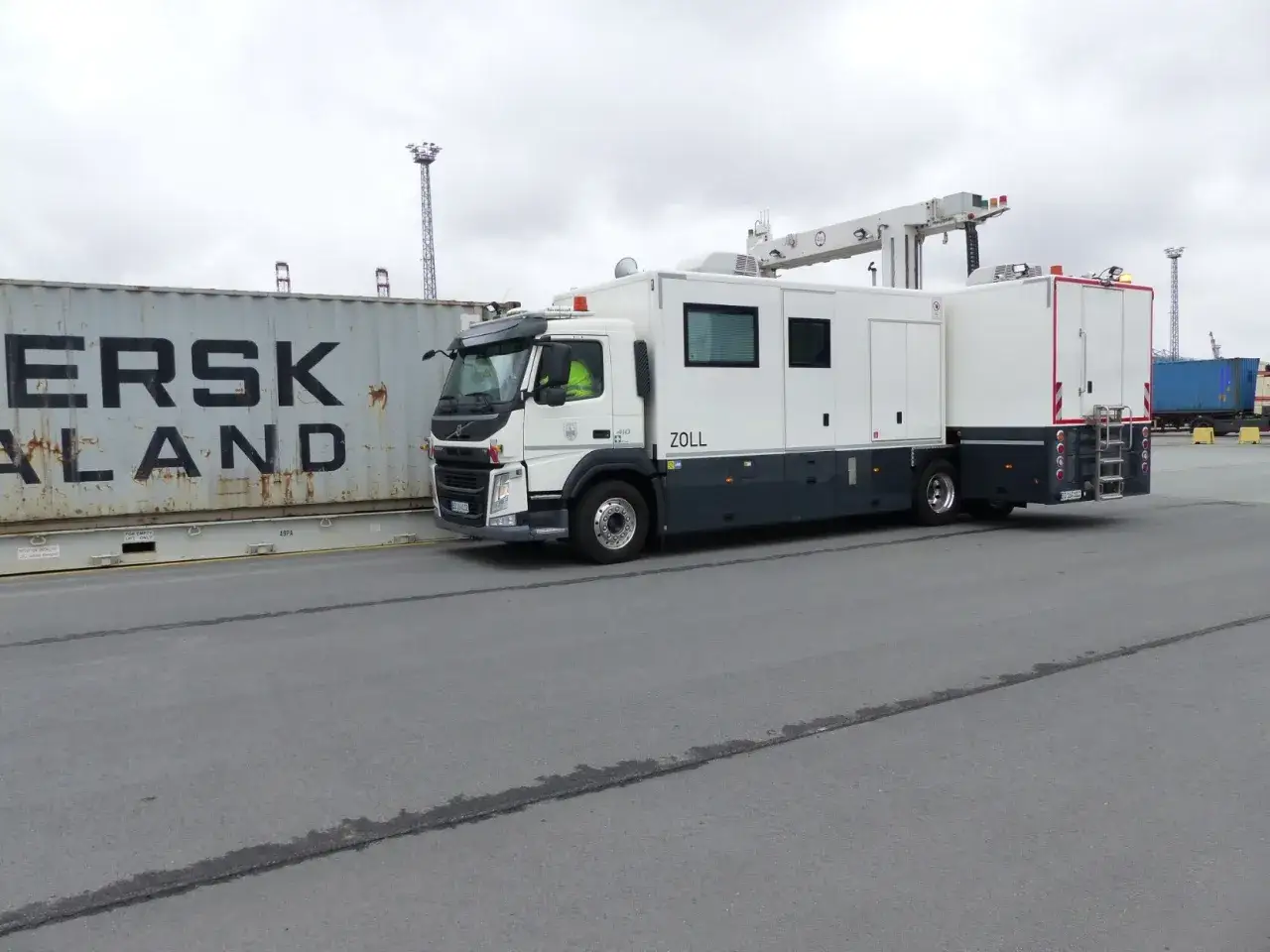 Ein Zoll-LKW mit Scanner-Aufbau steht neben einem Container.