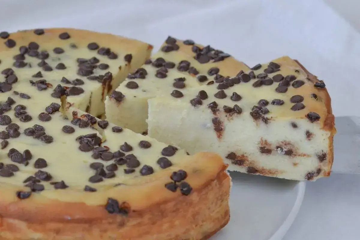 Una deliziosa torta ricotta e cioccolato, con tante gocce di cioccolato sparse sulla superficie e all'interno. Una fetta &egrave; appena stata tagliata.