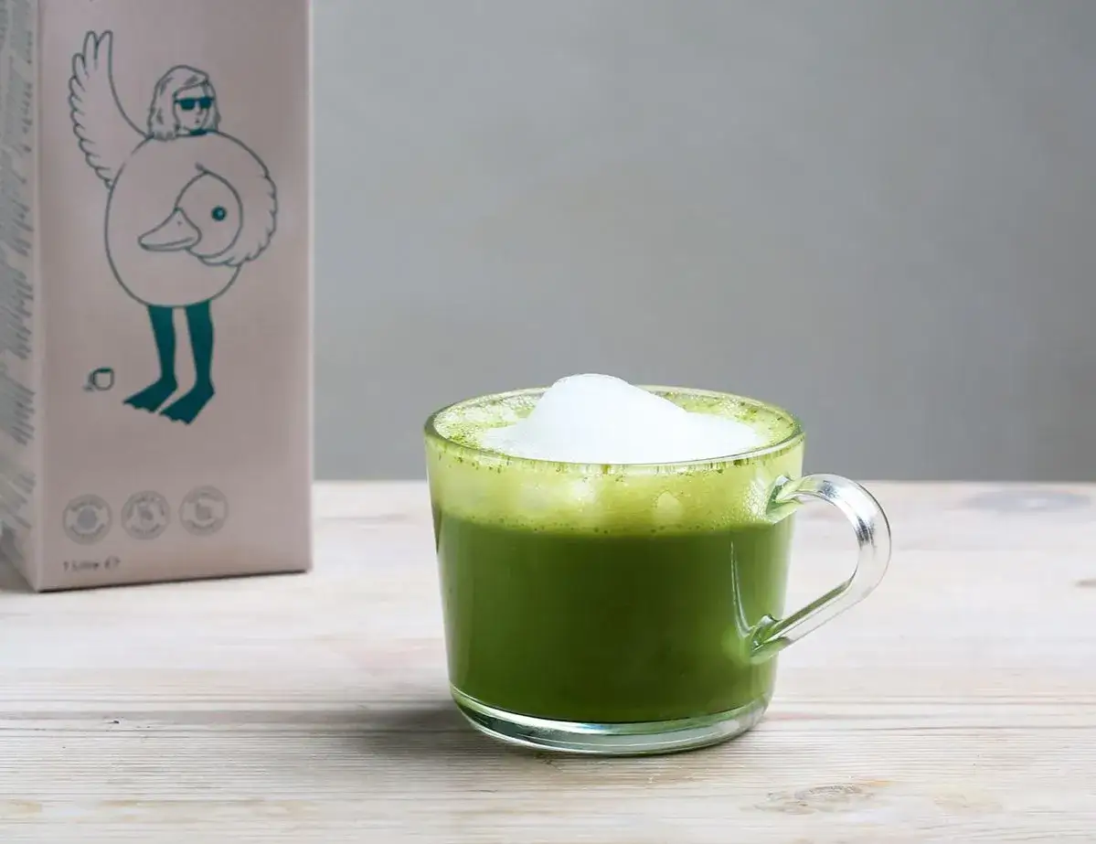 Un matcha lait d'avoine crémeux dans une tasse en verre, à côté d'une boîte au design original.