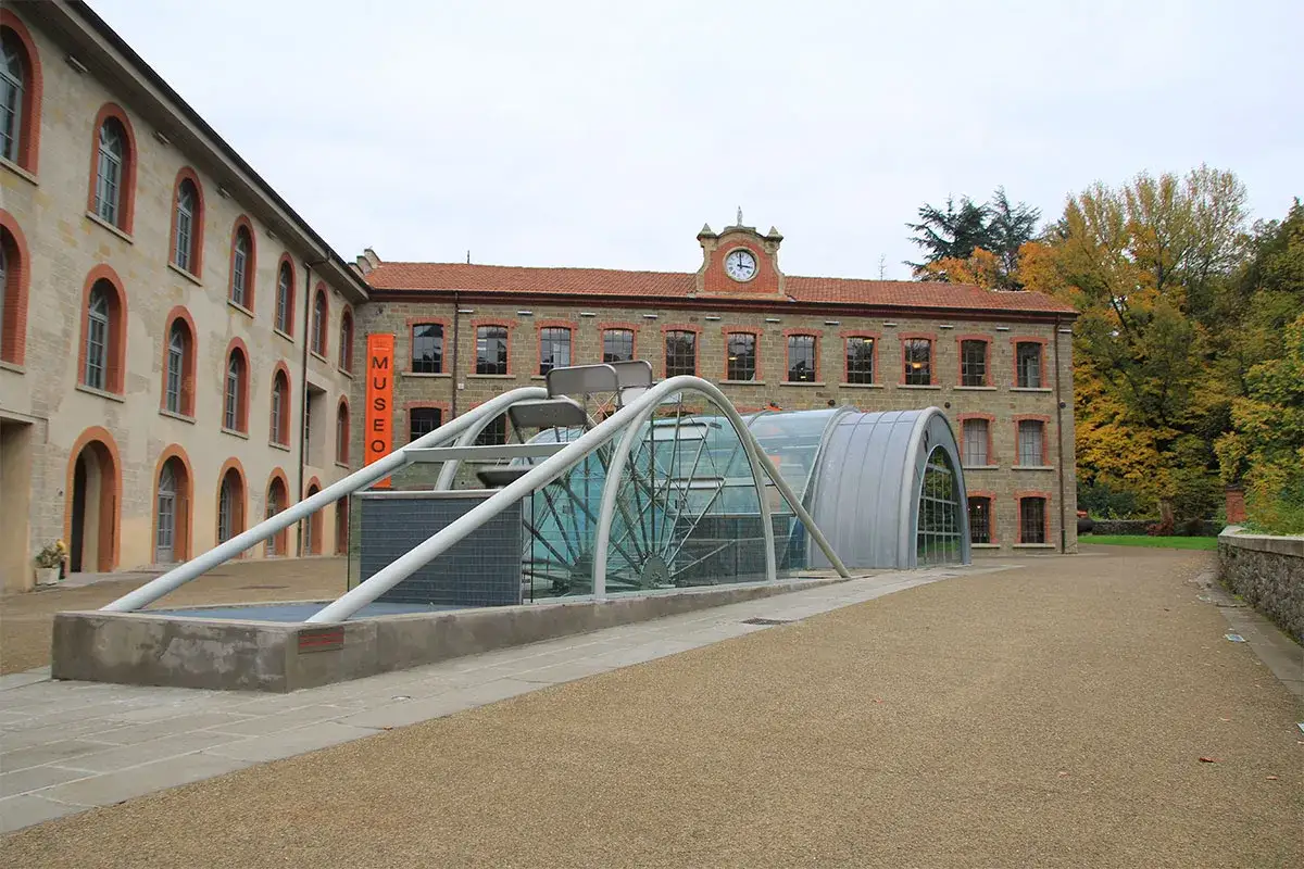 Edificio storico con insegna MUSEO, Arezzo. Struttura moderna in vetro e metallo con ruota.