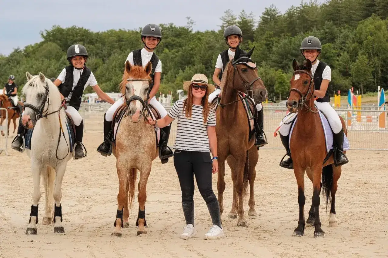 Des jeunes cavaliers et leur monitrice posent fi&egrave;rement apr&egrave;s avoir fait de l'&eacute;quitation.