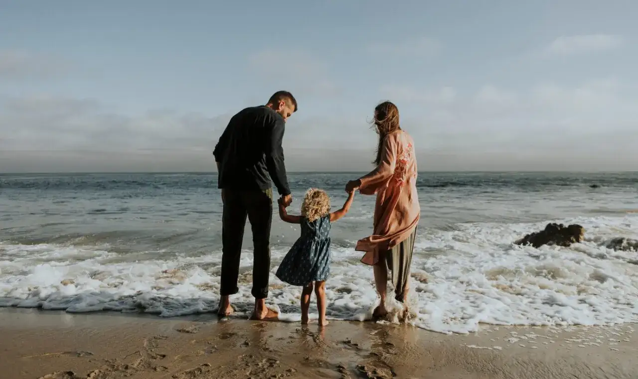 Rodzina na plaży, trzymająca się za ręce, marzy o tym, gdzie na wakacje 2026.