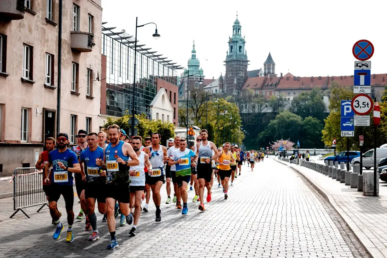 Uczestnicy biegu w Krakowie mijają zabytkowe kamienice i Wawel. W tle widać wieże zamku.