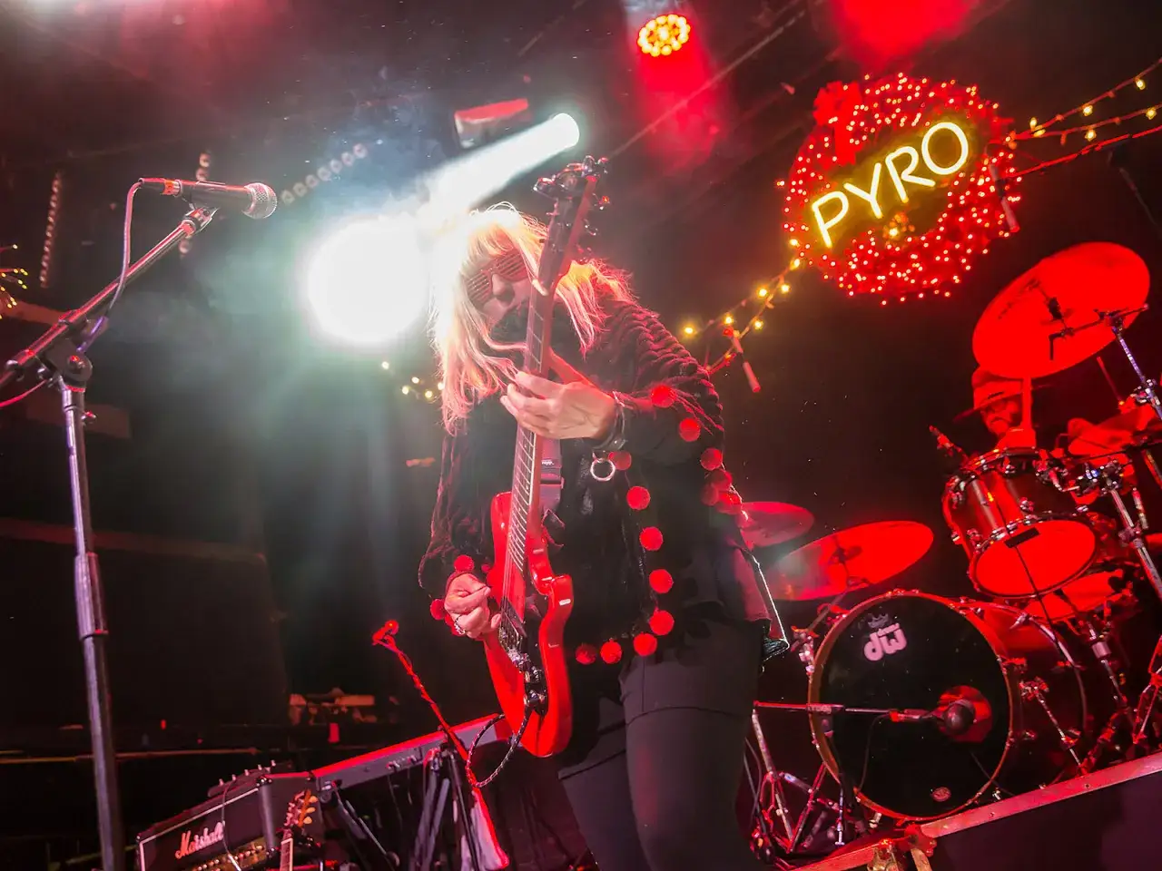 Une guitariste blonde, lunettes rouges, joue sur sc&egrave;ne avec son groupe punk des ann&eacute;es 90. Lumi&egrave;res vives, n&eacute;on 