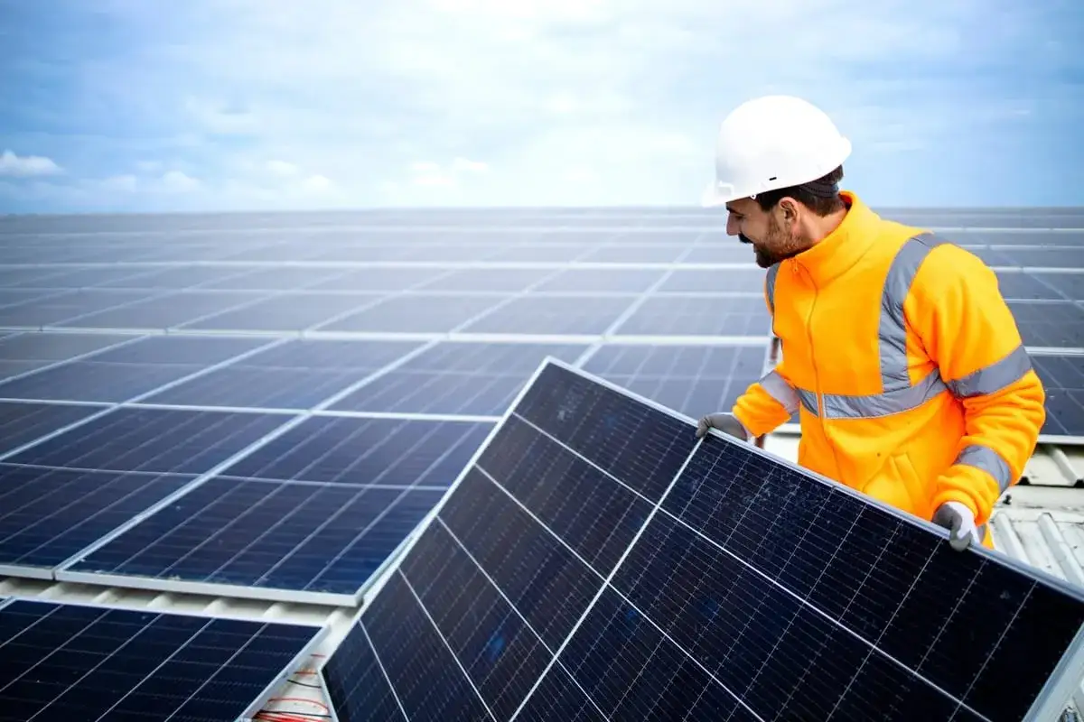 T&eacute;cnico de placas solares instala un panel en un tejado lleno de paneles bajo un cielo azul.