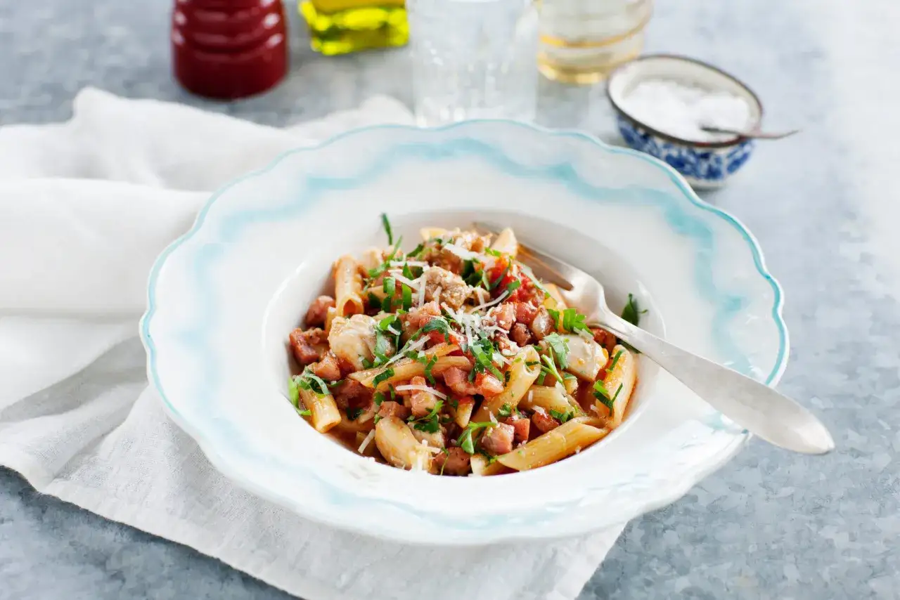 En tallrik med penne pasta, kyckling och t&auml;rnad pancetta, toppad med persilja och parmesan. Ett enkelt pancetta recept f&ouml;r en god middag.