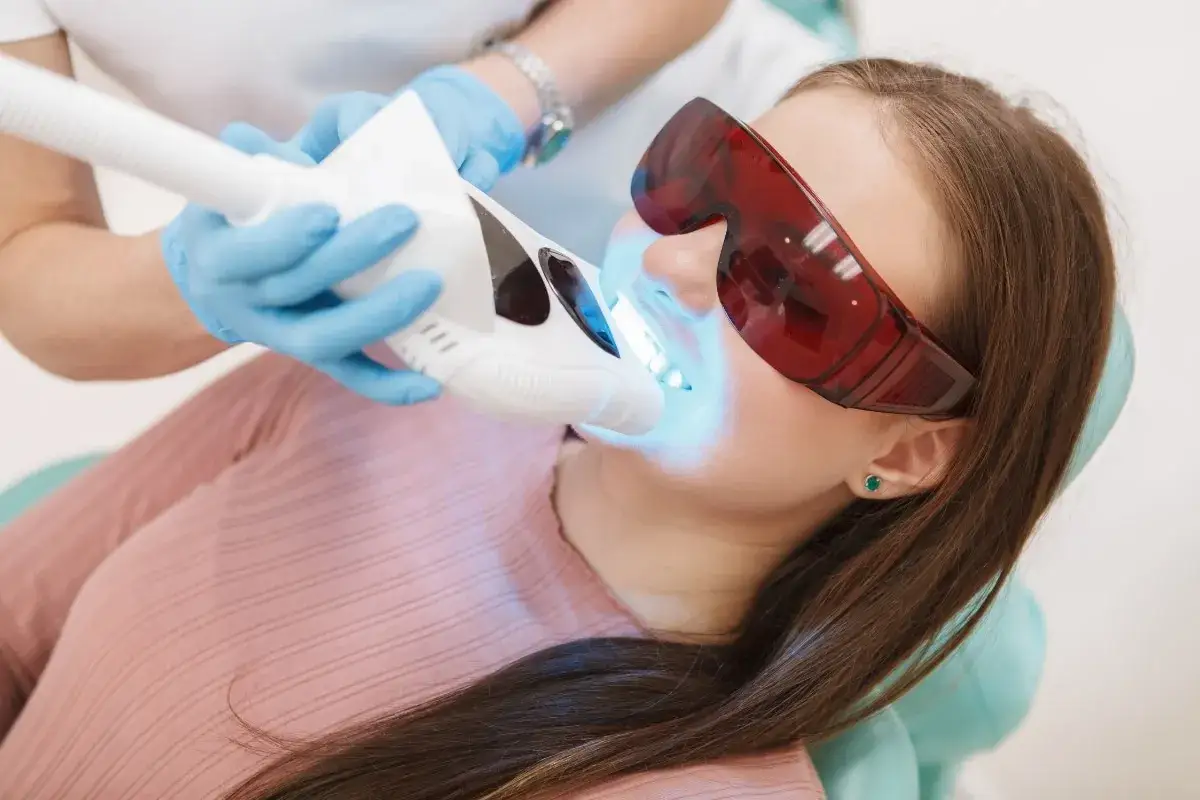 Pacjentka w okularach ochronnych przechodzi laserowe leczenie zębów. Niebieskie światło lasera rozjaśnia jej uśmiech.