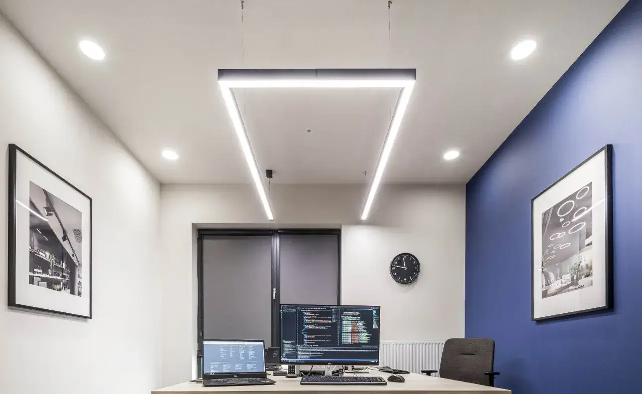 Bureau moderne avec postes informatiques, éclairage conforme à l'article R4223-13 du code du travail, et décorations murales.