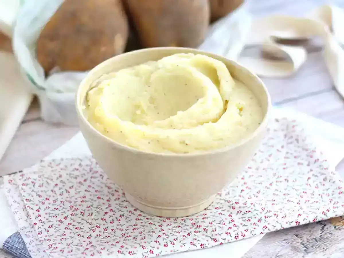 Krämig potatismos i skål, perfekt för ett enkelt potatismos recept. Bakom skymtar råa potatisar.