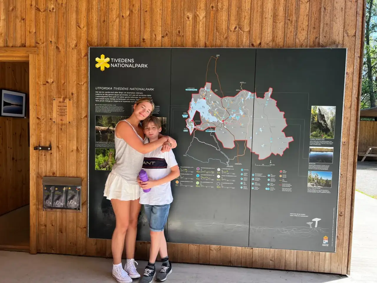 Två barn, en flicka och en pojke, står framför en karta över Tivedens nationalpark.