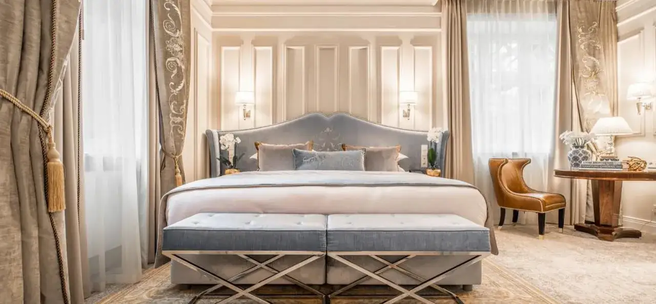 Elegancki executive room z dużym ł&oacute;żkiem, ozdobnymi zasłonami i stylowym fotelem.